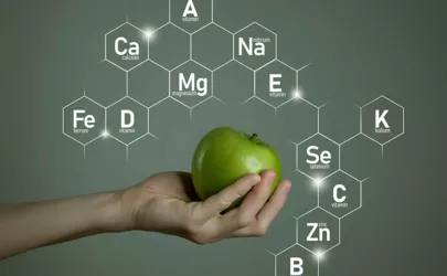 Frauenhand hält grünen Apfel, Mikroelement-Symbole in molekularen Sechsecken auf grauem Hintergrund.
