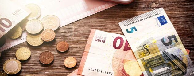 Ein Stapel Euro-Banknoten und -Münzen auf einem Holztisch.