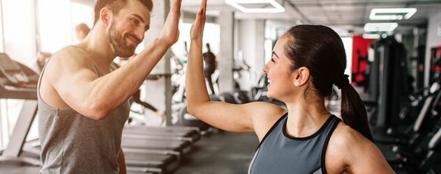 zwei sportliche Personen geben sich lachend einen High Five in einem Fitnessstudio