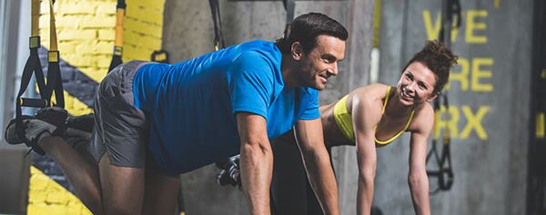 Ein Mann und eine Frau machen ein Trx-Training in einem Fitnessstudio.