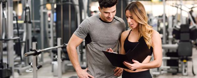 Ein Mann und eine Frau in einem Fitnessstudio, die auf ein Klemmbrett schauen.