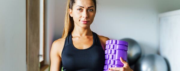 Eine junge Frau hält einen lila Gymnastikball in einem Fitnessstudio.