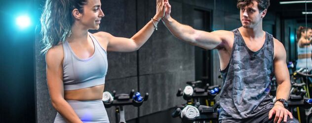 eine Frau und ein Mann geben sich ein High Five nach dem Radtraining im Fitnessstudio