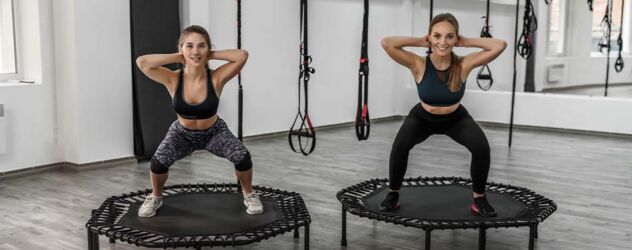 zwei junge Frauen in Fitnesskleidung, die Übungen auf dem Trampolin im Fitnessstudio machen