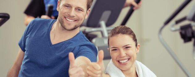 Ein Mann und eine Frau geben in einem Fitnessstudio Daumen nach oben.