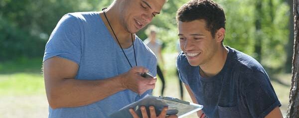 Zwei junge Männer schauen in einem Park auf ein Tablet.