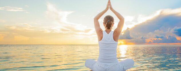 Yoga Pose, eine Frau in Schneidersitz mit den Armen über ihren Kopf zusammengefaltet, sitz auf einem Steg am Meer bei Sonnenuntergang