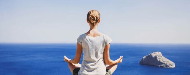 Eine Frau meditiert auf einem Berg mit Blick auf den Ozean.