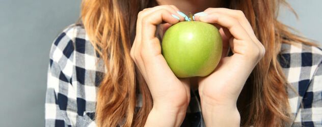 Eine Frau hält einen grünen Apfel in ihren Händen.