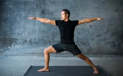 Mann, der vor einem dunklen Hintergrund Yoga praktiziert. Die Pose ist Krieger II, Virabhadrasana II.